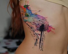 a watercolor tattoo on the side of a woman's stomach with a dandelion