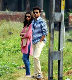 a man and woman standing next to each other in front of a pole with grass