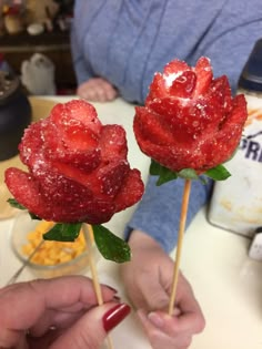 two strawberries with sugar on them are being held by someone's hands while sitting at a table