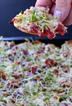 a person holding up a piece of pizza with toppings on it, in front of a pan