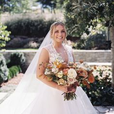 a woman in a wedding dress is holding a bridal bouquet and smiling at the camera