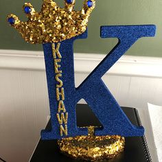 a blue and gold letter k with a crown on it's head sitting on top of a table