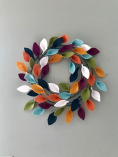 a multicolored felt wreath hanging on the wall in front of a white wall