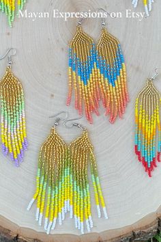 three pairs of multicolored beaded earrings on a piece of wood with grass in the background