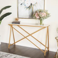 a white and gold console table with flowers in vases next to a painting on the wall