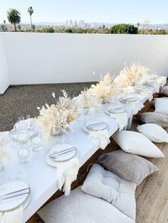 a long table with white plates and silverware on it is set for an outdoor dinner