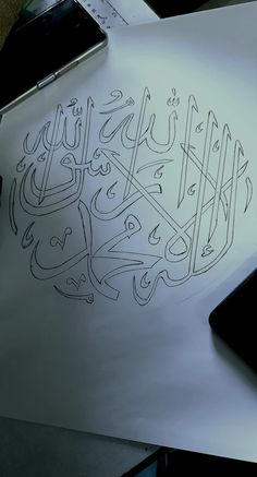 an arabic calligraphy is shown on top of a piece of paper with a cell phone next to it