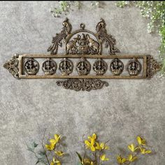 an ornate metal shelf with yellow flowers in front of it on a concrete wall next to potted plants