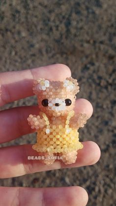 a tiny teddy bear made out of beads on someone's hand in the street