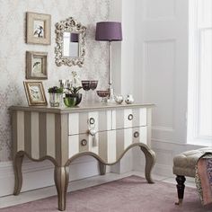 a white dresser sitting next to a window with pictures on the wall and a purple lamp