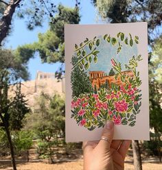 a hand holding up a card with an image of a castle in the background and flowers