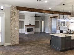 an empty kitchen and living room in a new construction home with wood floors, exposed brick fireplace, and white painted walls