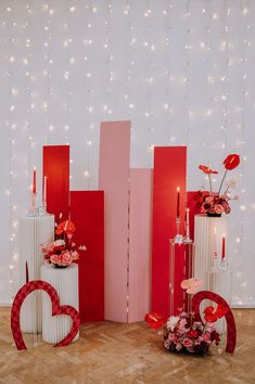 two tall white vases with flowers and candles in front of a wall decorated with lights