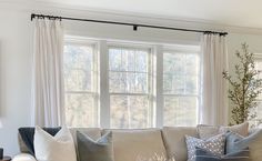 a living room filled with lots of furniture next to a large white window covered in curtains