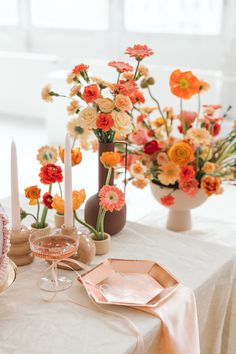 the table is set with candles, plates and vases filled with colorful flowers on it