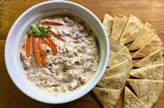 a white bowl filled with dip and tortilla chips on top of a wooden table