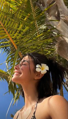 a woman standing under a palm tree with a flower in her hair and looking up at the sky