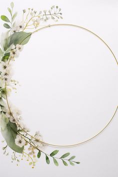 a circle frame with white flowers and greenery around it on top of a white surface