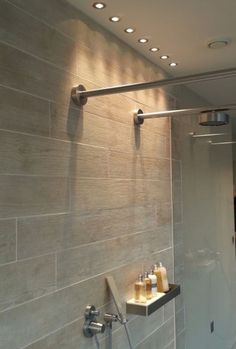 there is a shower with some soaps on the shelf next to it and lights above