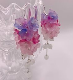 two pink and purple glass beads hanging from silver earwires on a clear vase