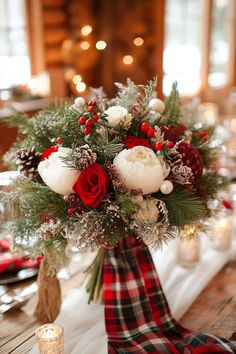 a christmas centerpiece with red and white flowers, greenery and pine cones on a wooden table