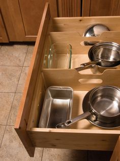 an open drawer with pots and pans in it on the floor next to wooden cabinets