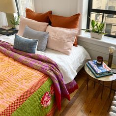 a bed with many pillows on top of it next to a lamp and window sill