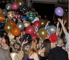 a group of people standing around each other with balloons in the air and confetti on their hands