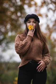 a woman holding a yellow flower in her mouth and looking at the camera while standing outside