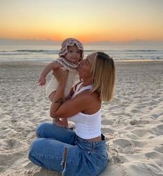 a woman sitting on top of a sandy beach holding a baby