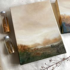 two paintings are sitting on a table next to some dried flowers and spices in glass jars