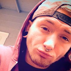 a man wearing a hoodie and piercing on his nose is taking a selfie