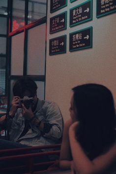 a man and woman sitting in front of a window taking pictures with their cell phones