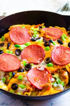 a skillet filled with pepperoni, black olives and green peppers on top of a table