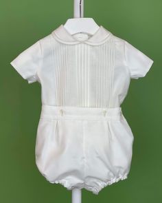 An elegant two-piece set for baby boys to wear during any special occasion. The top has a peter pan collar, handmade pleats, and short sleeves; it has buttons on the back for closure. The bottom is bubble-shorts with buttons on the sides for closure and an elastic band on the back. The interior, or lining, is made with cotton fabric, while the exterior is with off-white organza. Dry clean 2 piece set Interior: 100% cotton; exterior: 100% polyester Made in Spain Final Sale Elegant Fitted Sets With Pintucks, Elegant Cream Short Sleeve Sets, Classic Fitted Short Sleeve Sets, Elegant White Short Sleeve Sets, Fitted Short Sleeve Sets For First Communion, Classic Short Sleeve Sets For Baptism, White Short Sleeve Formal Sets, Elegant Short Sleeve Baptism Sets, Baptism Outfits For Boys