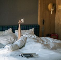 a woman laying in bed with her arms up and holding a coffee cup above her head