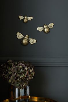 three brass bee decorations on the wall above a table with a vase full of flowers