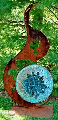 a metal sculpture sitting on top of a wooden base in the grass next to trees