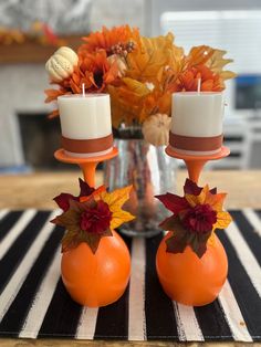 two candles are sitting on top of an orange vase with fall leaves and flowers in it