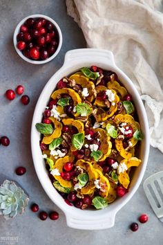 a white bowl filled with food next to some cranberries and oranges on a table