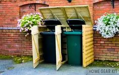 two trash cans sitting next to each other in front of a brick wall with flowers