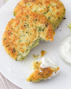 two crab cakes on a white plate with a small bowl of ranch dressing next to it