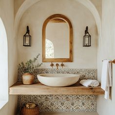 a bathroom sink sitting under a mirror on top of a counter next to a potted plant