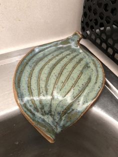 a green bowl sitting on top of a metal sink next to a black grate