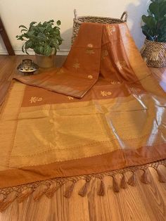 Blended Silk (cotton & silk) in a beautiful tawny brown shade with golden floral motifs all over the length of the saree and solid gold zari border. The fabric is a blend of cotton and silk- very soft and comfortable. It has a fall like crepe and looks just as royal as a benarasi.Condition: NewFabric: Cotton & SilkLength: 5.5 metres Fall & Pico : Saree comes with fall and pico Blouse: Saree comes with running blouse piece that is already cut. Customized stitching: available upon requ Brown Chanderi Dupatta With Traditional Patterns, Gold Cotton Silk Saree With Traditional Patterns, Brown Chanderi Traditional Wear, Brown Chanderi Traditional Wear For Festivals, Brown Chanderi Dupatta With Traditional Drape, Brown Dupatta With Zari Work In Traditional Drape, Brown Handloom Chanderi Dupatta, Brown Chanderi Dupatta With Cutdana, Brown Chanderi Handloom Dupatta