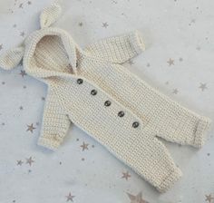 a crocheted baby sweater laying on top of a white sheet with silver stars