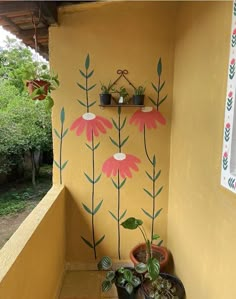 two potted plants on the side of a yellow wall with flowers painted on it