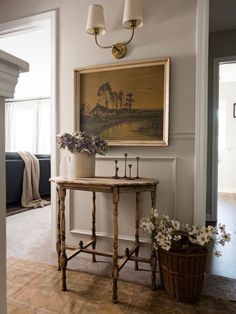 a painting hangs on the wall next to a table with flowers and two candles in it