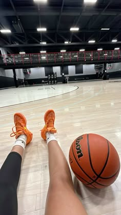 a person's feet resting on a basketball in an indoor gym