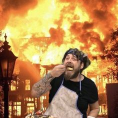 a man with an apron eating food in front of a large fire that is raging